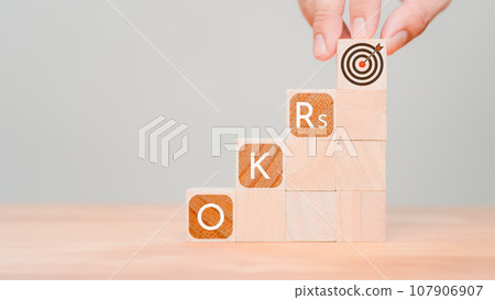 Man holding a wooden cube block with goal icon and OKR or Objectives and Key Results text. Business target and drive business and performance. 107906907