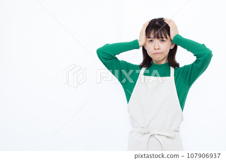 一位 30 多歲的家庭主婦在白色背景前低著頭，憂心忡忡 107906937