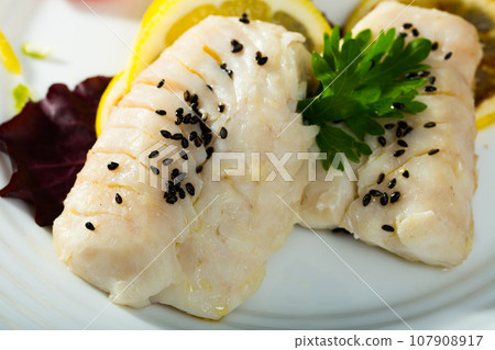 Codfish prepared on steam and served with greens and lemon 107908917