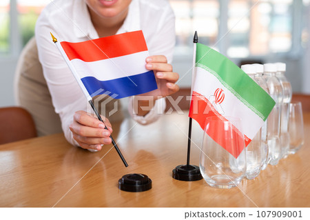 Little flag of Iran on table and flag of Netherlands put next to it by young woman Little flag of Iran on table and flag of Netherlands put next to it by young woman 107909001
