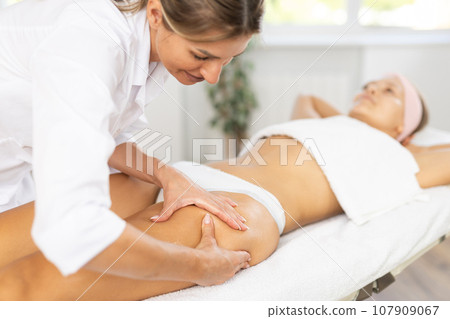 Female masseur performs patting during spa procedure of front zone thigh for girl Female masseur performs patting during spa procedure of front zone thigh for girl 107909067