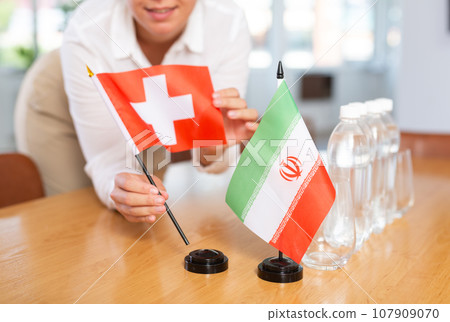 Little flag of Iran on table and flag of Switzerland put next to it by young woman 107909070