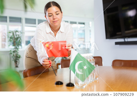 Young woman putting flags of China and Pakistan on table in office Young woman putting flags of China and Pakistan on table in office 107909229