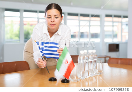 Positive young woman putting little flag of Greece on table next to the flag of Iran Positive young woman putting little flag of Greece on table next to the flag of Iran 107909258