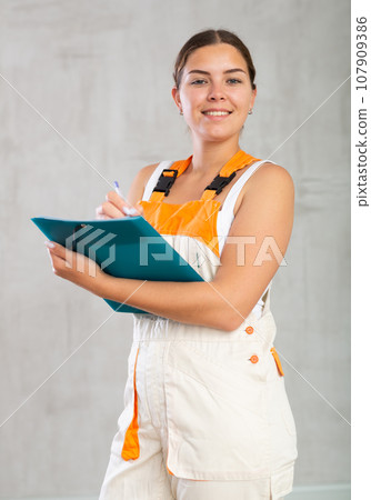 Young woman in work overalls making notes Young woman in work overalls making notes 107909386