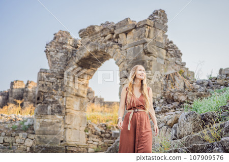 Woman tourist explores Aspendos Ancient City. Aspendos acropolis city ruins, cisterns, aqueducts and old temple. Aspendos Antalya Turkey. turkiye 107909576