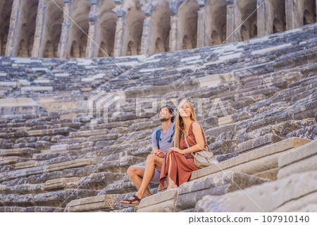 Happy couple man and woman tourists explores Aspendos Ancient City. Aspendos acropolis city ruins, cisterns, aqueducts and old temple. Aspendos Antalya Turkey. turkiye Happy couple man and woman tourists explores Aspendos Ancient City. Aspendos acropolis city ruins, cisterns, aqueducts and old temple. Aspendos Antalya Turkey. turkiye 107910140