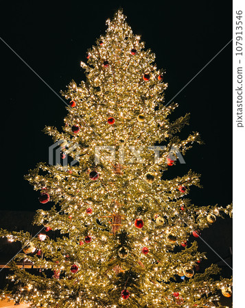 Christmas tree decorated with colorful balls with luminous garlands against a dark sky 107913546