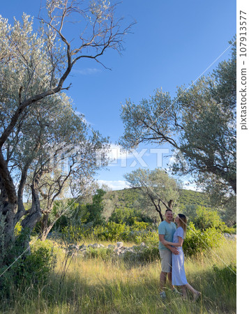 Smiling man and woman standing near green tree in garden 107913577