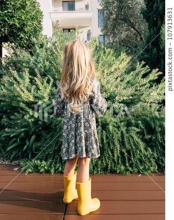 Little girl looks at a juniper bush blooming with pink flowers. Back view Little girl looks at a juniper bush blooming with pink flowers. Back view 107913631