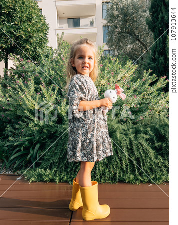 Little girl with a toy hare stands near a flowering juniper bush Little girl with a toy hare stands near a flowering juniper bush 107913644