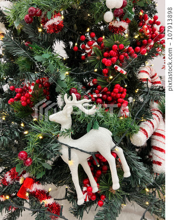 Christmas tree decorated with a figurine of a deer, red berries and garlands 107913898