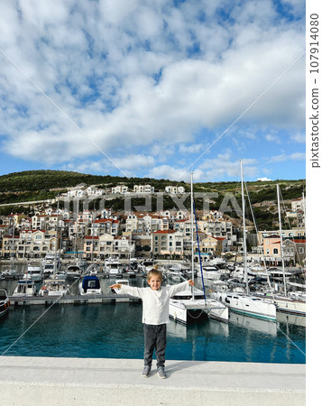 Little girl stands on the pier against the backdrop of moored yachts Little girl stands on the pier against the backdrop of moored yachts 107914080