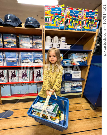 Little girl with a basket of books stands in a bookstore Little girl with a basket of books stands in a bookstore 107914101