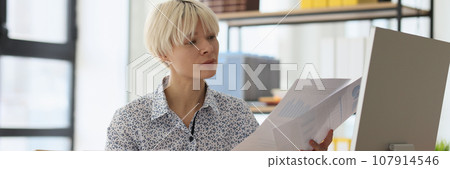 Curious blonde woman compares information reading papers 107914546