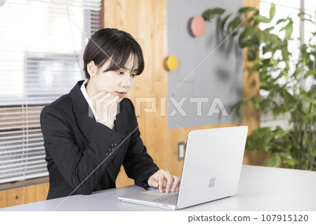 一名 20 多歲的女性一邊看著筆記型電腦一邊思考 107915120