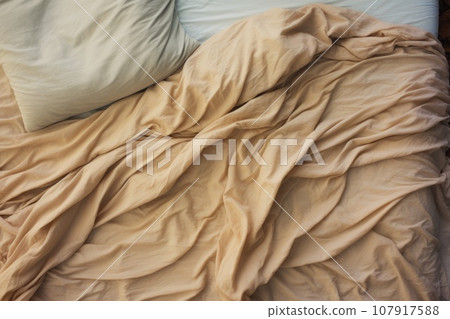Top view of an unmade beige bed with a crumpled sheet, blanket and pillows Top view of an unmade beige bed with a crumpled sheet, blanket and pillows 107917588