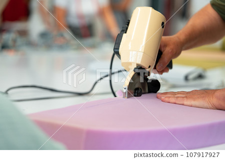 Hands of a furniture master cut a piece of foam with foam cutting machine Hands of a furniture master cut a piece of foam with foam cutting machine 107917927