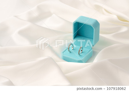 White gold earrings in blue jewelry box on silk background 107918062