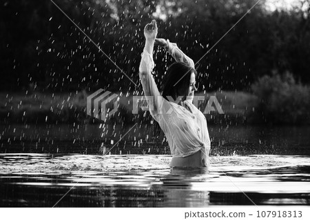 Happy blonde woman having fun in sunny park smiling, fooling around, laughing. Slow Motion. Beautiful caucasian girl dancing under the summer rain. wet hair and clothes. enjoying with drops. 107918313