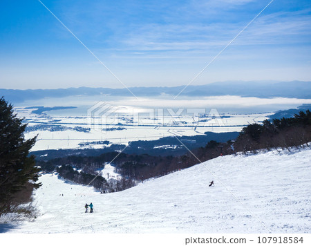 A snowy town seen from the ski resort and a lake half covered in a sea of clouds (Fukushima Prefecture, Inawashiro) 107918584