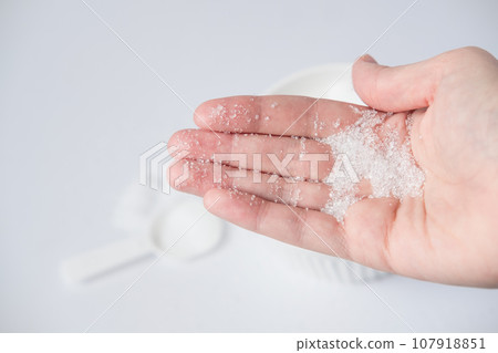 Epsom salt in hand for bath on white background. Useful salt for relaxation in the bath. Magnesium salt 107918851