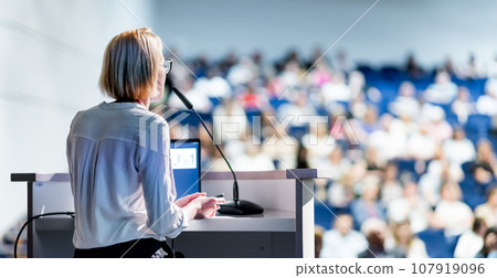 Female speaker giving a talk on corporate business conference. Unrecognizable people in audience at conference hall. Business and Entrepreneurship event Female speaker giving a talk on corporate business conference. Unrecognizable people in audience at conference hall. Business and Entrepreneurship event 107919096