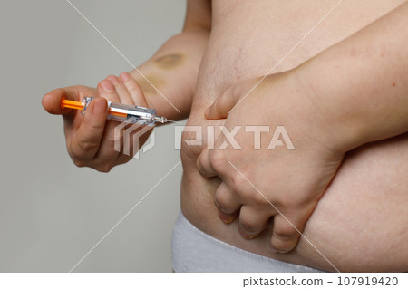 Overweight woman applying medicine injection into her stomach closeup Overweight woman applying medicine injection into her stomach closeup 107919420