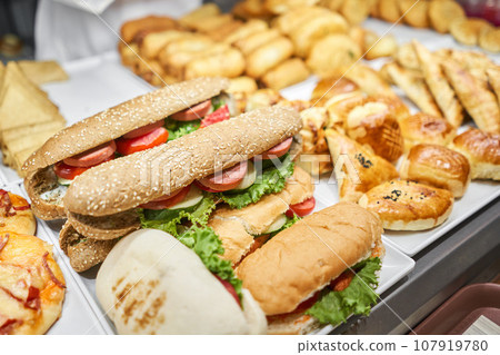 Fresh sandwiches, pies and pizza to choose from in the window of a cafe, buffet or self-service cafe. Croissant with ham and cheese. Hot pastries lie on the shelf in the cafe. Buns in the store. Fresh sandwiches, pies and pizza to choose from in the window of a cafe, buffet or self-service cafe. Croissant with ham and cheese. Hot pastries lie on the shelf in the cafe. Buns in the store. 107919780
