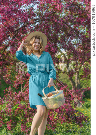 young woman in park enjoying a picnic. She holds an iron basket with fruits young woman in park enjoying a picnic. She holds an iron basket with fruits 107919963