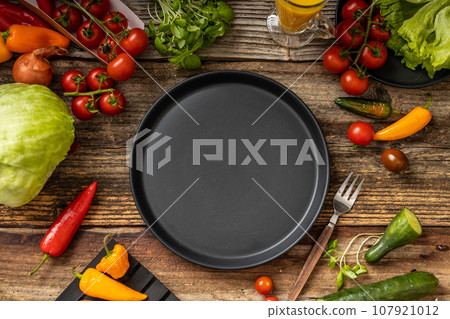 Black plate on wooden rustic table with vegetables Black plate on wooden rustic table with vegetables 107921012