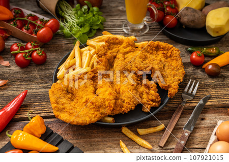 Golden bown crispy pork with fried fries in a black plate with helthy vegetables on the wooden table Golden bown crispy pork with fried fries in a black plate with helthy vegetables on the wooden table 107921015