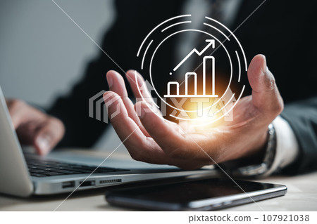 Businessman hand holds an arrow graph on his palm with laptop computer, embodying the concept of development to success and growing growth. Corporate future growth plan in hand is the focus. 107921038