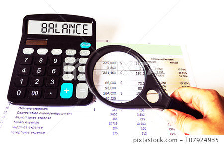 Calculator with the word BALANCE on display . Hand holding a magnifying glass over financial reports Calculator with the word BALANCE on display . Hand holding a magnifying glass over financial reports 107924935