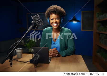 African American woman recording a blog in the studio, wearing headphones in front of a microphone, recording podcasts, blogging African American woman recording a blog in the studio, wearing headphones in front of a microphone, recording podcasts, blogging 107925112