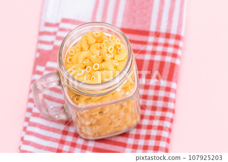 Uncooked Chifferi Rigati Pasta in Glass Jar on Checkered Red Towel Uncooked Chifferi Rigati Pasta in Glass Jar on Checkered Red Towel 107925203