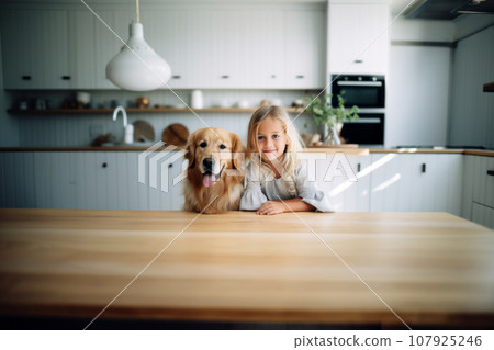 Teenage girl is preparing for breakfast at the kitchen table with a golden retriever dog in the kitchen. Cute baby and dog from home. 107925246