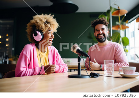 couple of smiling man and woman are writing a blog in the studio. An African American man and a woman have fun in the studio with microphones, headphones and a laptop while recording a vlog 107925380