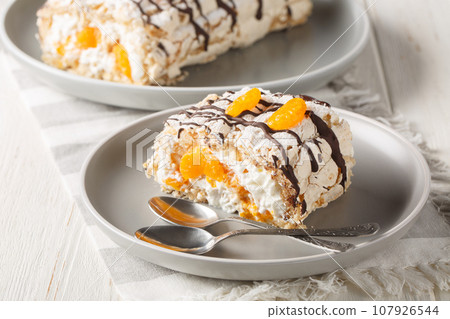 Delicious homemade Swedish dessert Budapest roll cake filled with whipped cream and mandarins close-up in a plate on the table. Horizontal 107926544