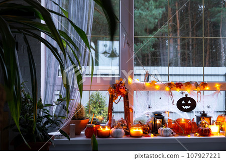 Festive decor of the house on the windowsill for Halloween in interior with homemade potted plants- pumpkins, Jack o lanterns, skulls, skeletons, candles and garland - cozy and terrible mood Festive decor of the house on the windowsill for Halloween in interior with homemade potted plants- pumpkins, Jack o lanterns, skulls, skeletons, candles and garland - cozy and terrible mood 107927221