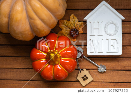 Cozy layout on a wooden background of slats with pumpkins, autumn leaves, a house and keys - autumn mood, Halloween, housing, relocation, mortgage, insurance. Cozy layout on a wooden background of slats with pumpkins, autumn leaves, a house and keys - autumn mood, Halloween, housing, relocation, mortgage, insurance. 107927253