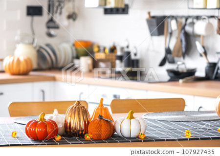 Decor of white classic kitchen with pumpkins, garlands, latern for Halloween and harvest with figurine of house. Autumn mood in home interior, modern loft style. real estate, insurance, mortgage Decor of white classic kitchen with pumpkins, garlands, latern for Halloween and harvest with figurine of house. Autumn mood in home interior, modern loft style. real estate, insurance, mortgage 107927435