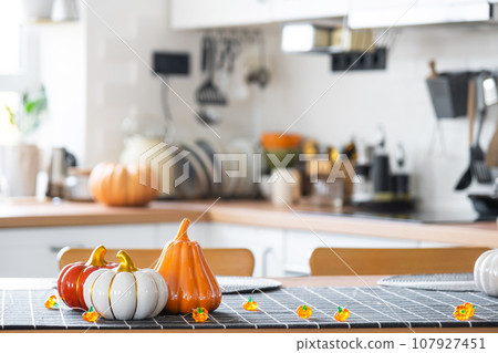 Decor of white classic kitchen with pumpkins, garlands, latern for Halloween and harvest with figurine of house. Autumn mood in home interior, modern loft style. real estate, insurance, mortgage Decor of white classic kitchen with pumpkins, garlands, latern for Halloween and harvest with figurine of house. Autumn mood in home interior, modern loft style. real estate, insurance, mortgage 107927451
