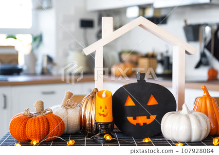 Decor of white classic kitchen with pumpkins, garlands, jack latern for Halloween and harvest with figurine of house. Autumn mood in home interior, modern loft style. real estate, insurance, mortgage 107928084