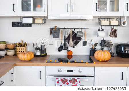Decor of the white classic kitchen with pumpkins for Halloween and harvest. Autumn mood in the home interior, modern loft style. Decor of the white classic kitchen with pumpkins for Halloween and harvest. Autumn mood in the home interior, modern loft style. 107928085