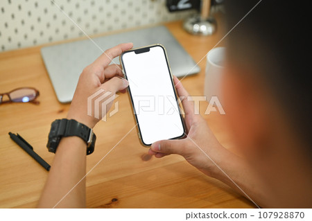 Close up male hands using smartphone at working desk searching data or chatting online 107928870