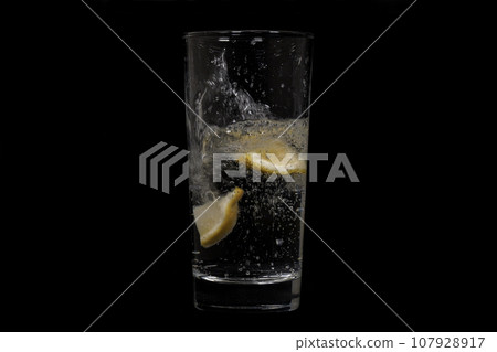 Close-up footage of soda and lemons pouring into glass on black background. Close-up footage of soda and lemons pouring into glass on black background. 107928917