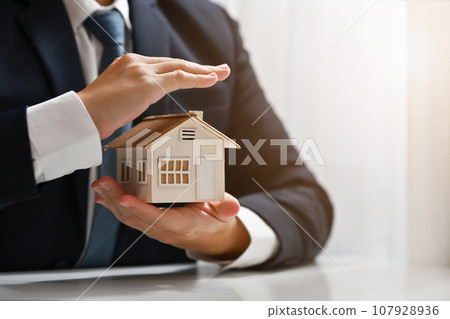 Businessman protecting house model with hands. Real estate and property Insurance concept Businessman protecting house model with hands. Real estate and property Insurance concept 107928936