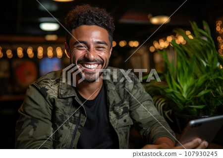 Cheerful smiling African American man in casual clothes holding smartphone sits at the table in cafe. Positive successful entrepreneur, small business owner works online. Remote work concept. Cheerful smiling African American man in casual clothes holding smartphone sits at the table in cafe. Positive successful entrepreneur, small business owner works online. Remote work concept. 107930245