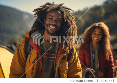 Happy African American couple in the mountains against the backdrop of a tent camp. Young international family is engaged in a mountain hike. Active lifestyle, tourism and vacation concept. Happy African American couple in the mountains against the backdrop of a tent camp. Young international family is engaged in a mountain hike. Active lifestyle, tourism and vacation concept. 107930271